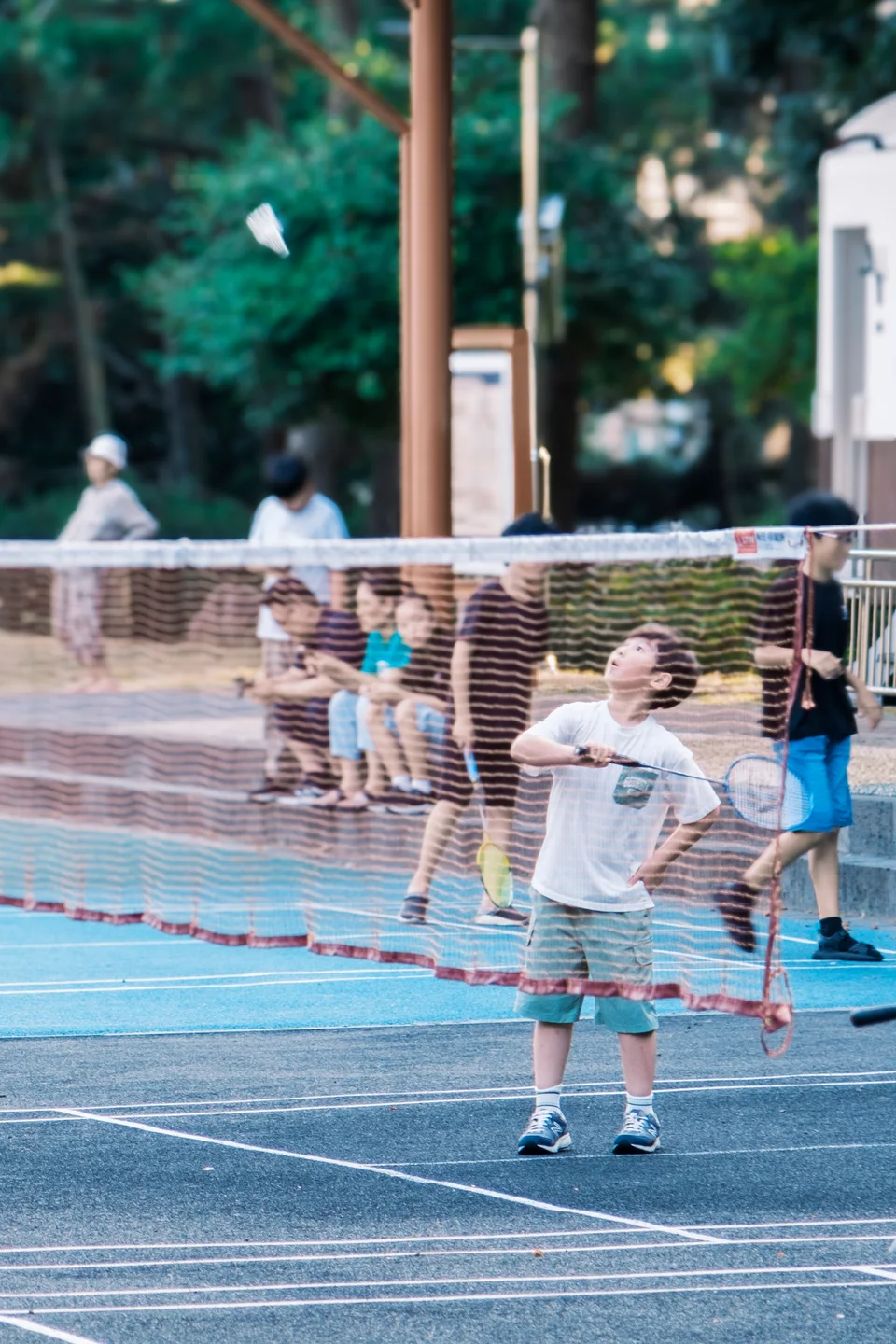 Child looking up at a shuttlecock on a badminton court